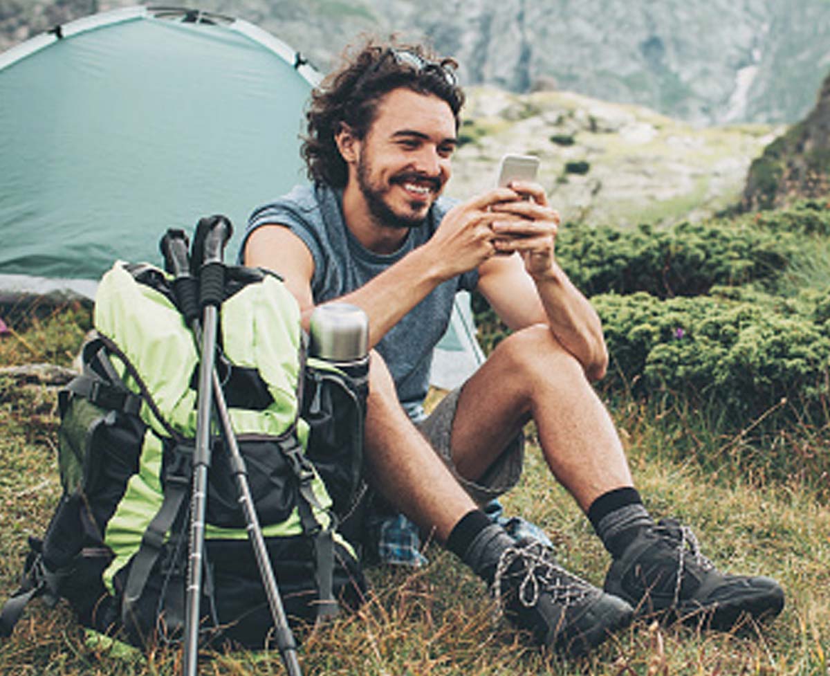 A man checking his MeMail email account on his phone while camping in the mountains.