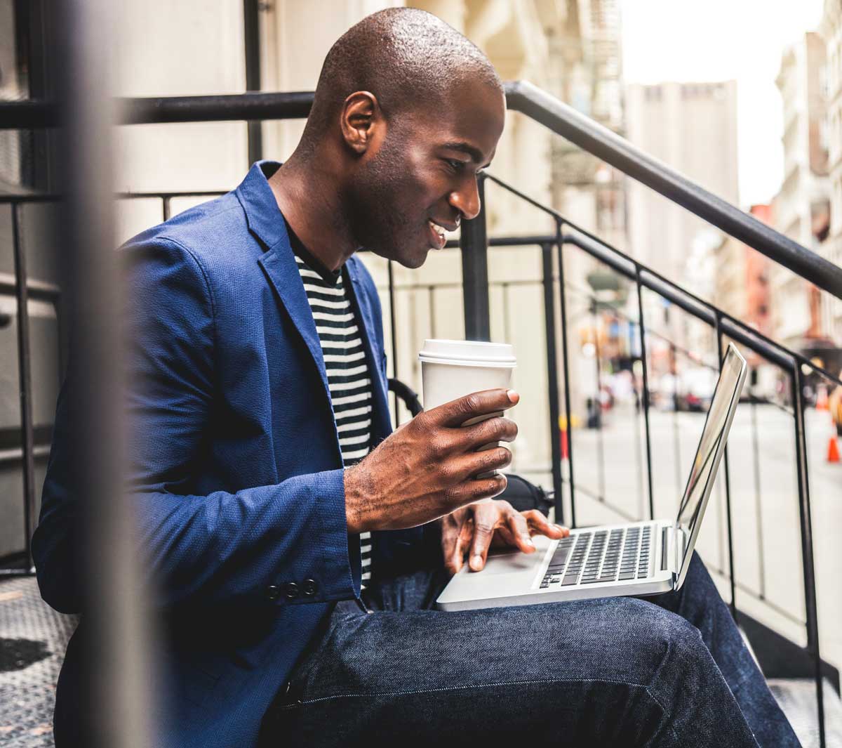 Guy Checking his email and drinking coffee outside on steps